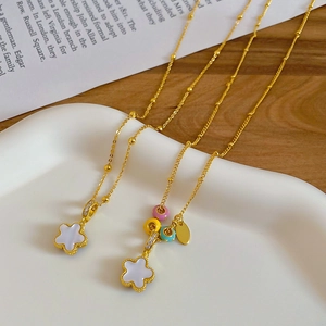 Close-up of golden flower pendant necklace with white shell inlay and colorful enamel beads