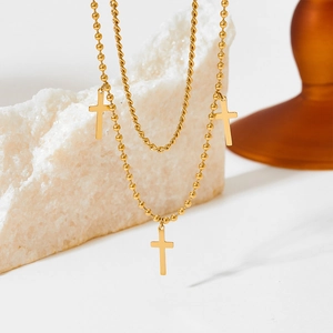 Macro detail of gold layered necklace featuring cable chain, bead chain and cross pendants