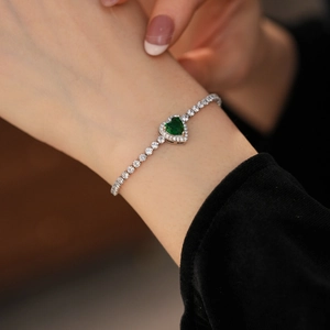 Close-up of heart-shaped green zircon tennis bracelet on woman's wrist with silver finish
