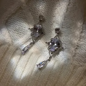 Macro shot of silver teardrop zircon earrings with vintage lace texture on knit background