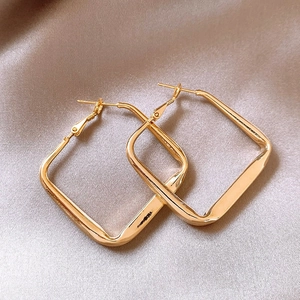 Detailed close-up of geometric square gold metal earrings on soft beige silk fabric
