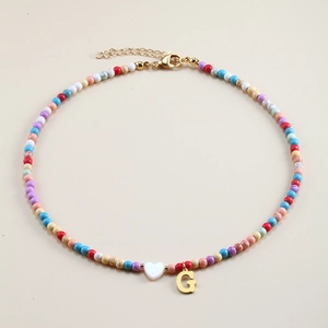 Detail of colorful beaded necklace with white heart bead and gold letter G pendant