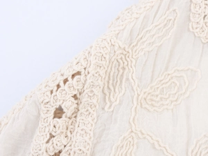 Detail of white crochet cardigan featuring leaf embroidery and textured bohemian fabric