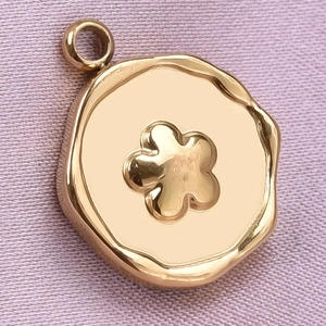 Close-up of golden irregular round pendant with embossed flower on purple fabric