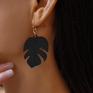 Close-up of black monstera leaf wooden earring with golden hook on model