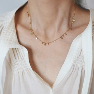 Close-up of gold beaded chain necklace with rectangular sequins on a model neck
