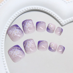 Lavender gradient press-on toenails with white floral patterns and golden shimmer