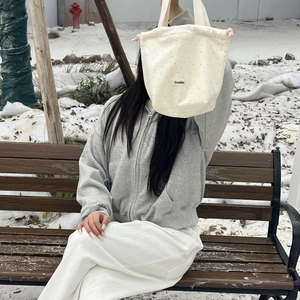 Detail view of a beige wool polka dot drawstring tote bag in a winter landscape