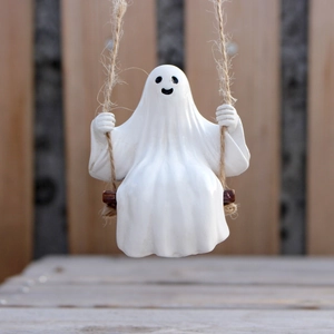 Detail of a white ceramic ghost sitting on a swing for Halloween outdoor tree decoration