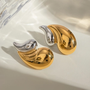 Macro view of geometric two-tone gold and silver earrings on a wavy white surface