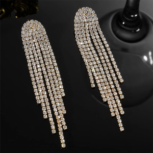 Detail of long gold tassel earrings with sparkling rhinestones on a dark surface