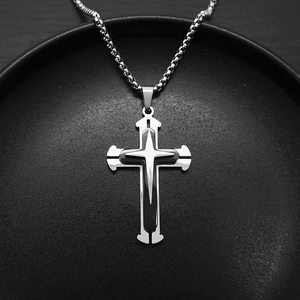 Macro shot of tiered silver and black cross pendant on a textured display plate