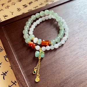 Detail of beaded lily of the valley bracelet with green jade-like beads and gold tassels