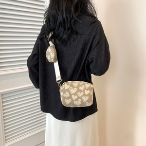 Detail of crossbody bag with wide strap and round coin purse featuring white heart patterns