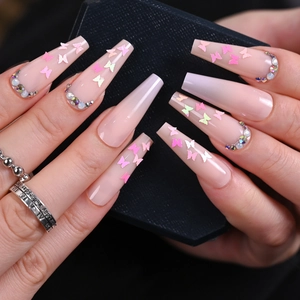 Close-up of long coffin fake nails in nude pink with butterfly charms and rhinestones