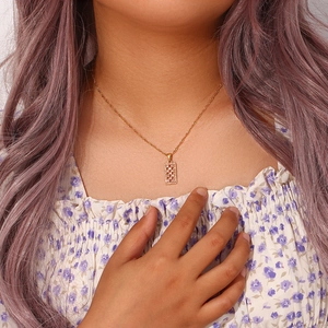 Detail of a gold rope chain necklace featuring a rectangular zircon pendant on a model