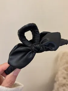 Dettaglio della pinza per capelli a fiocco in pelle nera con trama a grana fine