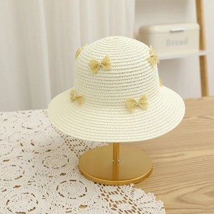 Close-up of beige woven straw hat with yellow lace bows on a gold metal display stand