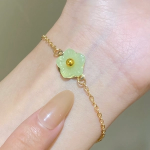 Detailed close-up of a delicate gold chain bracelet with a green flower petal pendant