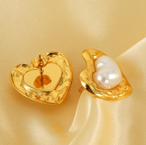 Detail of heart stud earrings with hammered gold texture and white pearl on satin