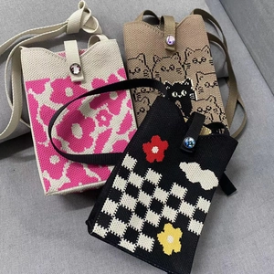 Three minimalist knitted crossbody phone bags with floral and cat patterns shown on a sofa