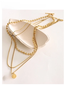Detailed view of layered gold titanium steel coin necklaces with OT clasp and coin pendants