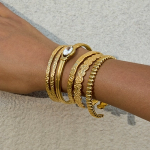 Dettaglio macro del set di bracciali dorati con diverse trame e cristallo marquise
