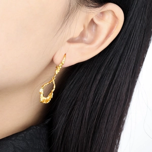 Golden irregular hollow earrings with molten metal texture on a female model's ear