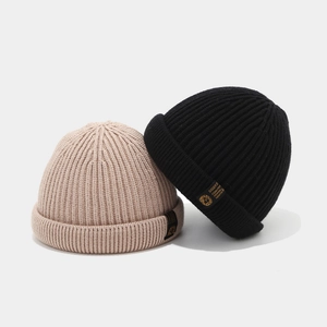 Détail de bonnets en maille côtelée beige et noir avec étiquettes latérales rétro