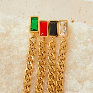 Detail of gold tassel earrings with baguette-cut emerald-colored stones on a stone background