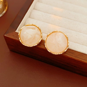 Detail of round cream earrings with textured gold rim in a luxury wooden jewelry box