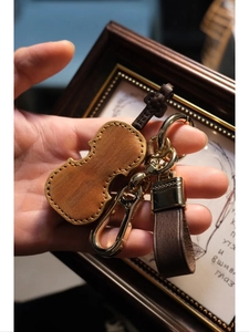 Detail of a brown leather violin keychain with gold hardware held in hand