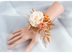 Gros plan du bracelet fleur avec rose ivoire, œillets orange et feuilles dorées