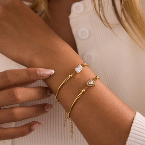 Close-up of 18K gold-plated bracelets featuring emerald and heart-cut cubic zirconia stones