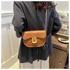 Brown PU leather saddle bag with gold buckle shown on a model in a cafe setting
