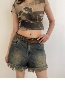 Detail of vintage embossed leather belt on distressed denim shorts with fringe