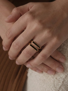 Detailed view of two stacked minimalist gold rings with black rectangular oil drip accents