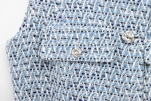 Close-up of blue tweed fabric texture with silver floral metal button and intricate weaving