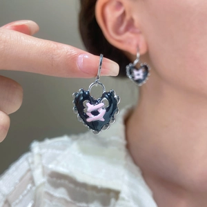 Macro shot of silver heart earrings with black enamel and pink cross ribbon detail