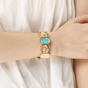 Close-up of golden enamel flower bangle worn by a model against white pleated fabric