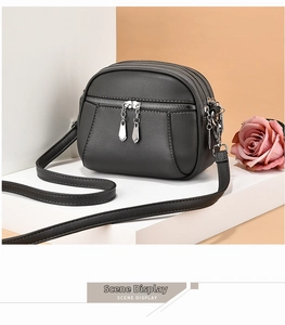 Detail of dark grey leather crossbody bag featuring triple zipper compartments and texture