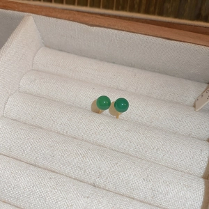 Close-up of elegant emerald green round stud earrings in a white velvet jewelry box