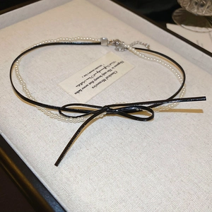 Detail of double-layer necklace with black leather bow and white pearl strand