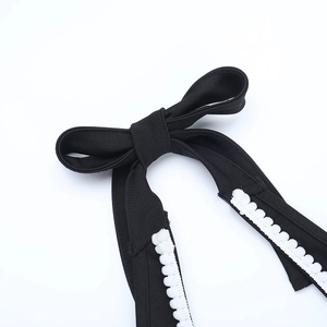 Détail de l'épaule d'une robe noire avec un nœud délicat et une bordure en dentelle blanche