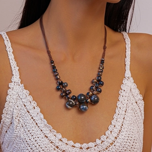 Détail de collier boho tissé avec perles bleu foncé sur un haut en crochet blanc