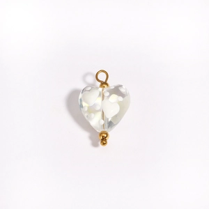 Detail of a transparent heart-shaped glass bead with golden metal ring and white pattern