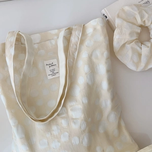 Flat lay of cream polka dot cotton tote bag with matching scrunchie and label detail