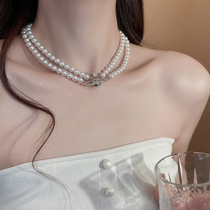 Detail view of a double-layer pearl necklace with a zircon Saturn pendant worn by a model