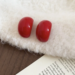 Macro shot of glossy Ancora red drop-shaped earrings resting on soft white faux fur fabric