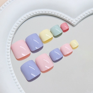 Colorful rainbow macaron press-on toenails with glossy finish on a mirrored surface